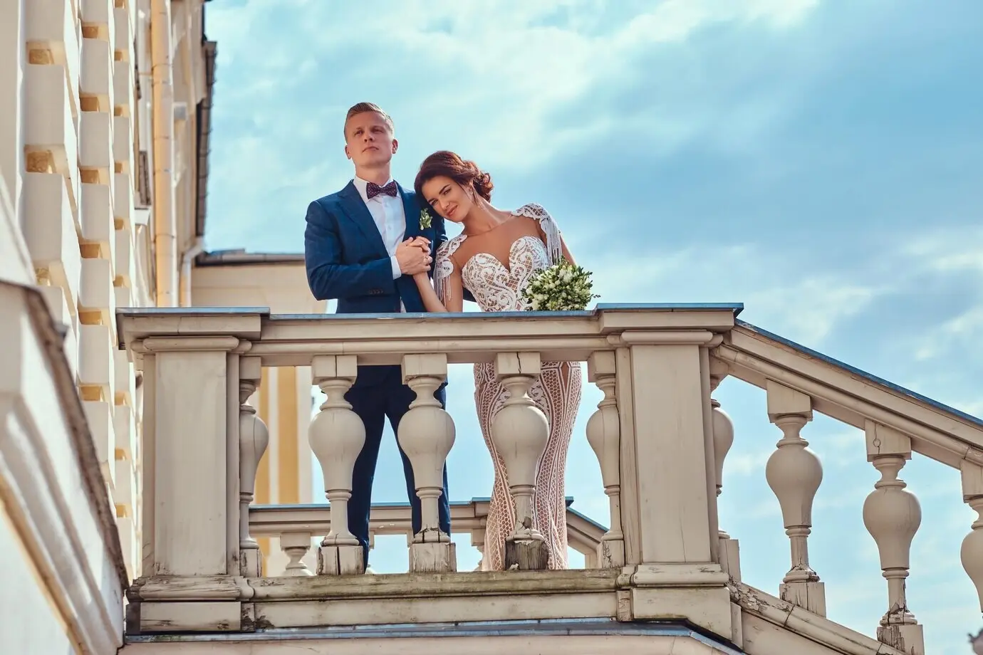 Porträt eines glücklichen frisch verheirateten Paares, das sich umarmt, während es auf der Treppe des schönen alten Palastes posiert.